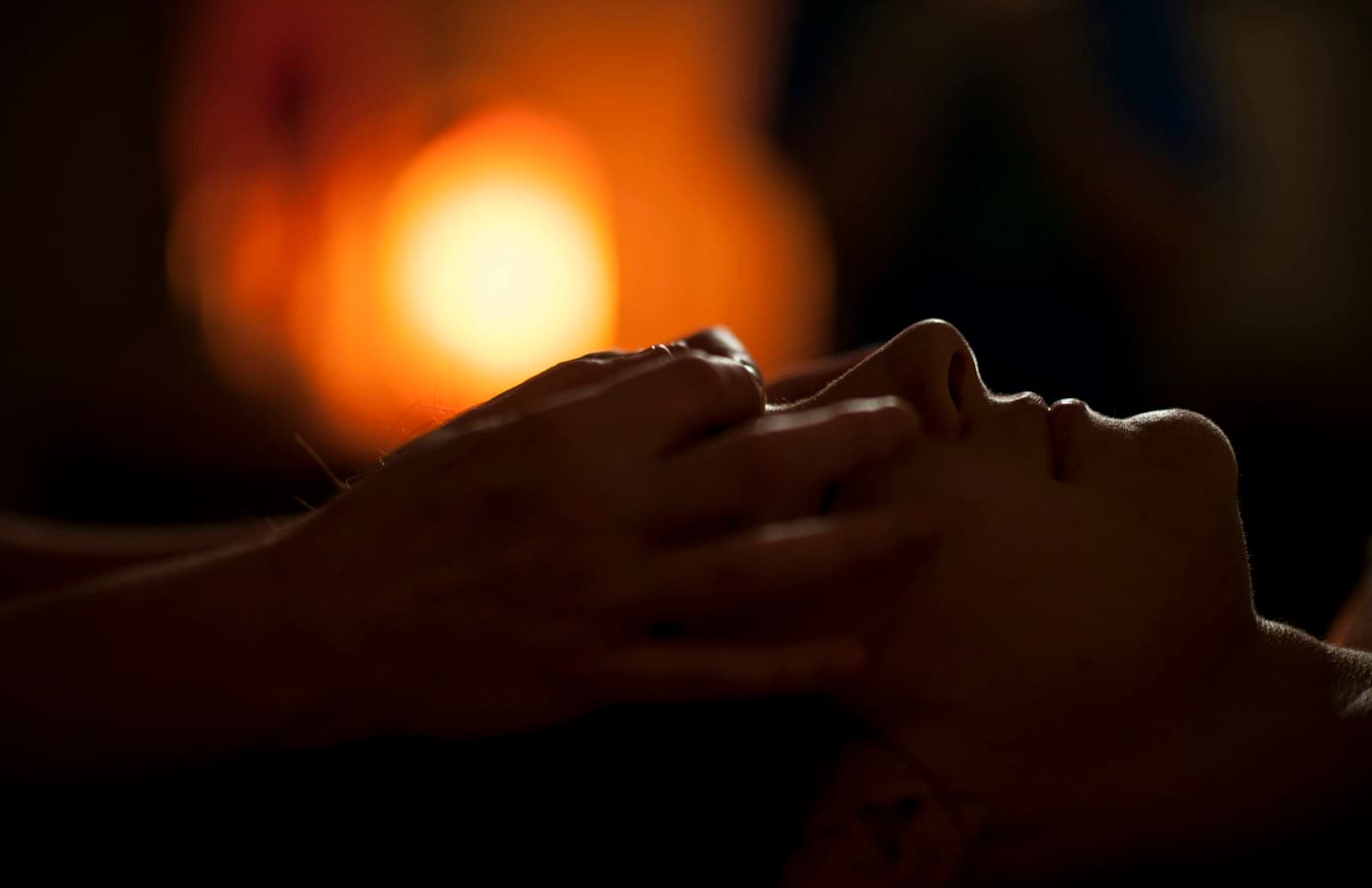 Hands giving a gentle head massage by warm candlelight