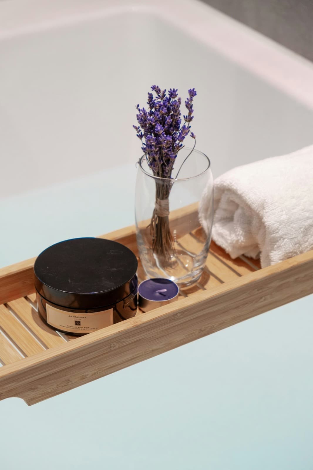 A bath tray with lavender, a candle and a rolled towel