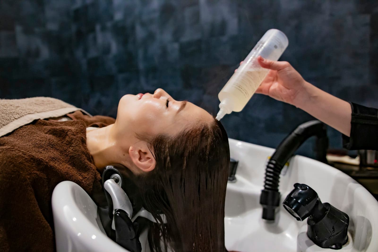 A therapist applying scalp treatment at a salon washbasin