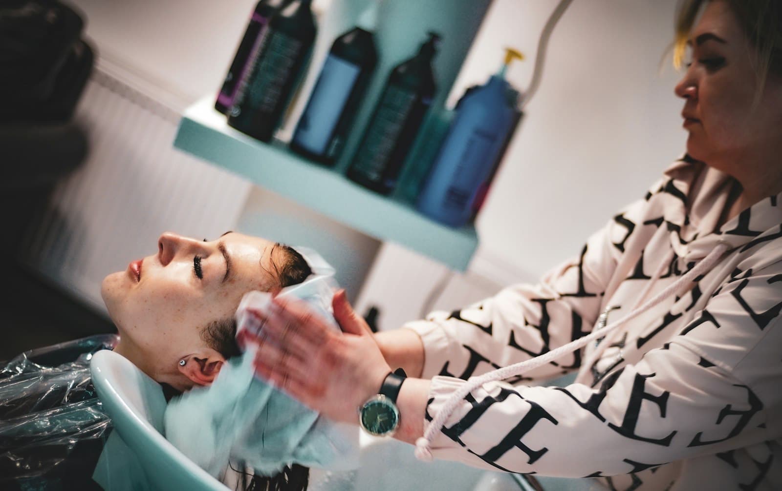 A client reclining at a salon backwash having their hair rinsed by a therapist